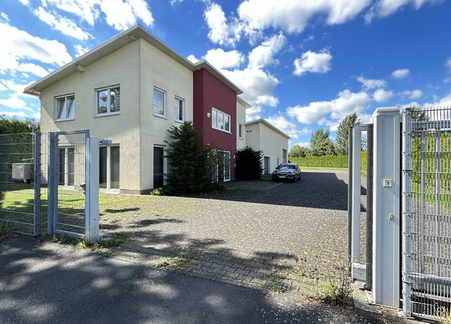 Blick auf eine leerstehende Gewerbeimmobilie mit gelber und roter Fassade sowie Pultdach.
